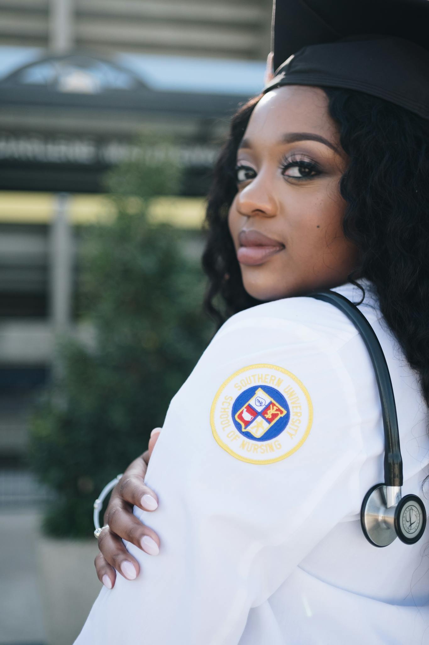 Confident nursing graduate posing outdoors in Baton Rouge with stethoscope and cap.